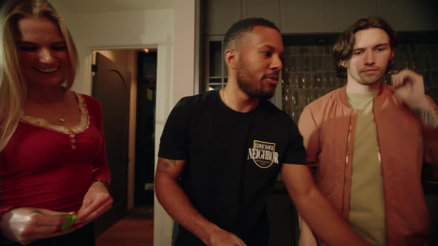 A group of diverse friends laugh and talk together while making a homemade pizza in a cozy kitchen