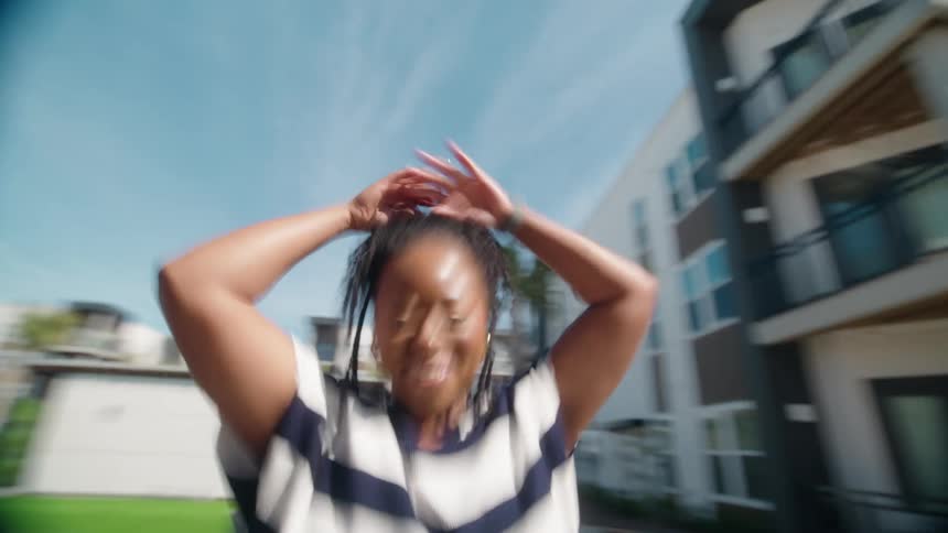 A dizzying slow-motion shot of a joyful Black woman spinning and dancing ecstatically in a sunny courtyard
