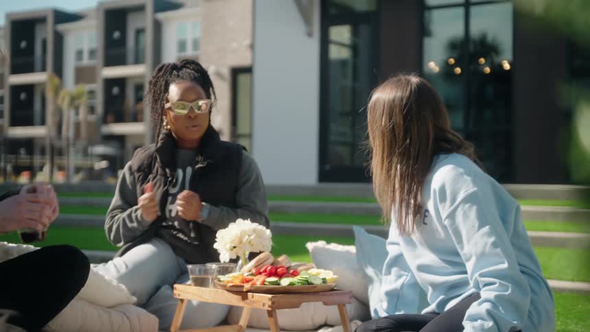 A group of diverse young friends enjoy a picnic on a sunny day in the common area of their apartment complex