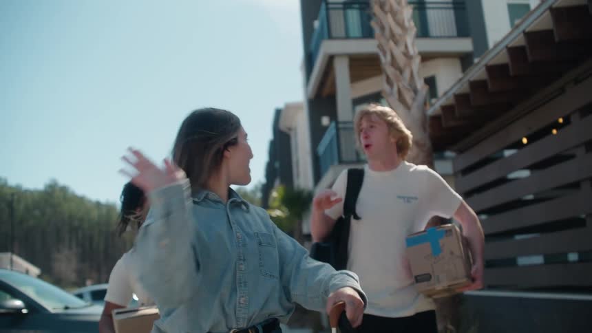 A diverse group of happy friends excitedly walk with boxes and luggage to move into their new apartment on a sunny day