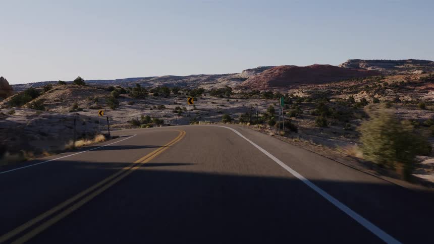 A first-person perspective of a drive along a winding road through a desert canyon landscape in the morning sun