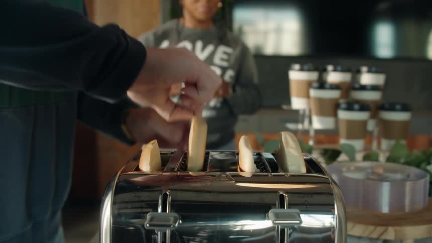A man in slow motion takes bagels out of a toaster as a woman watches in the background