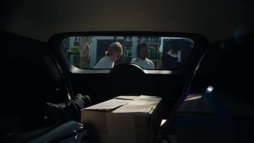 Friendly movers greet a happy resident and begin unloading boxes from a car trunk at a new apartment complex