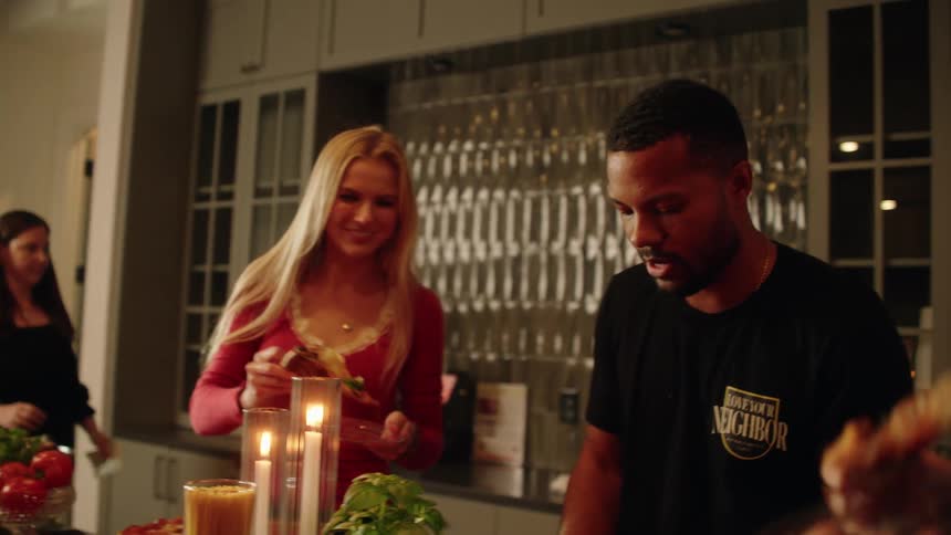 A diverse group of friends laugh and toast with pizza slices at a cozy, candlelit dinner party