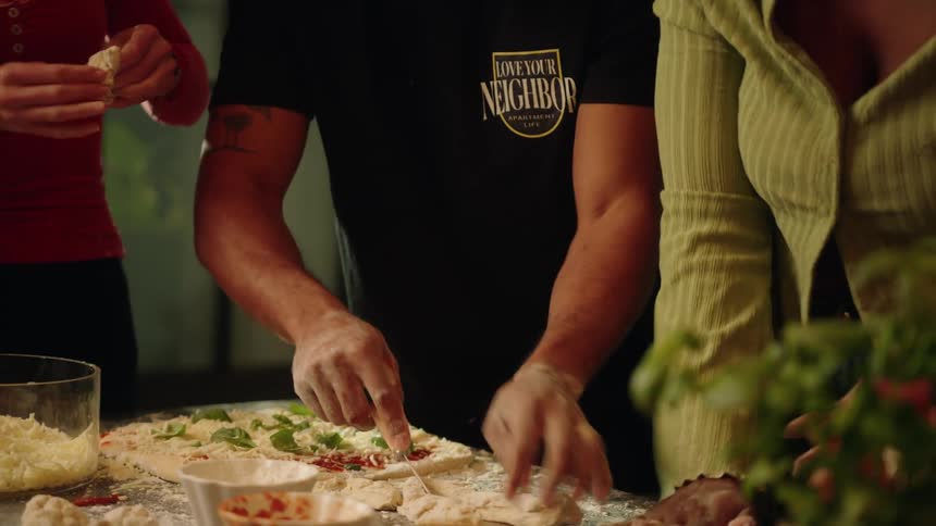 A group of diverse friends have a fun pizza night, laughing together as they prepare homemade dough and toppings in a cozy kitchen