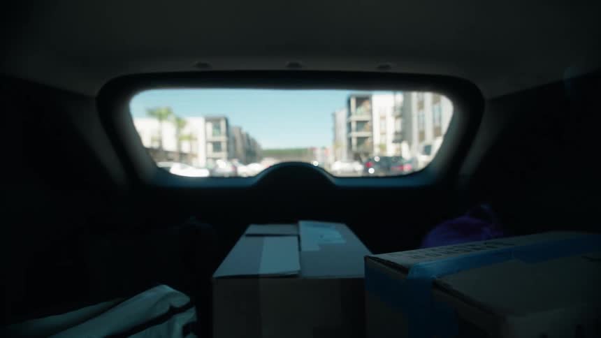 Blurry POV from the trunk of a car filled with moving boxes driving away from a modern residential neighborhood