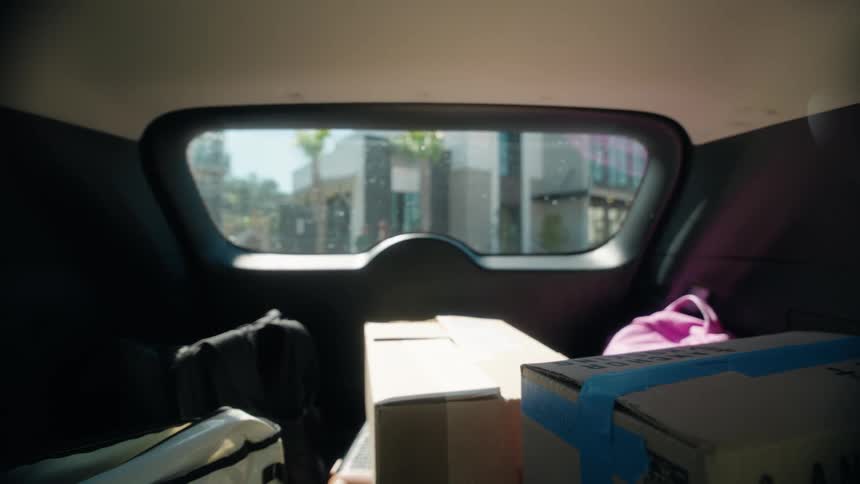 A point-of-view shot from the back of a moving car filled with boxes, journeying through a suburban neighborhood
