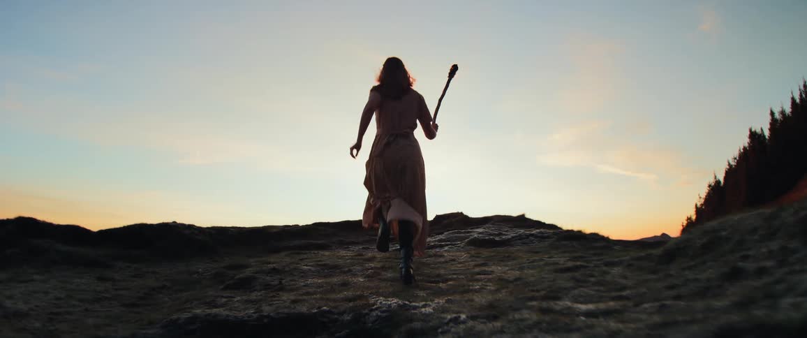 Dramatic slow motion of a woman in a long dress running with a lit torch toward the horizon at dusk