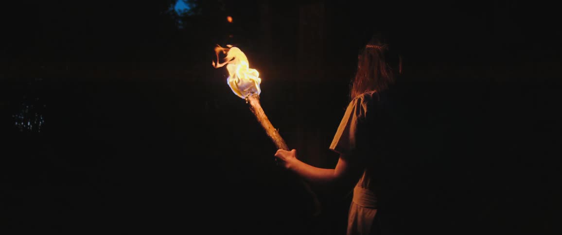 A mysterious figure holds a brightly burning torch, illuminating the darkness in a slow-motion cinemagraph