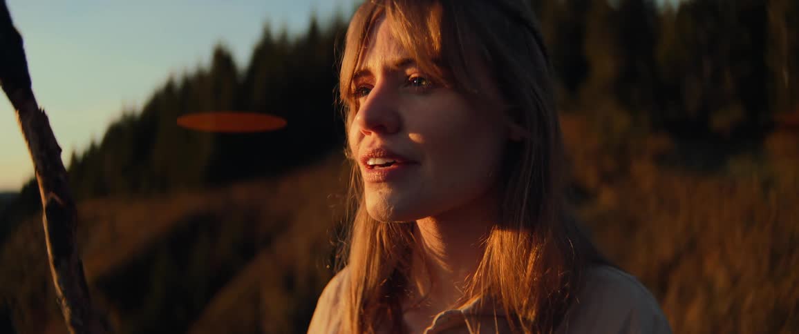 A close-up portrait of a thoughtful young woman looking out with emotion, bathed in the warm glow of golden hour light