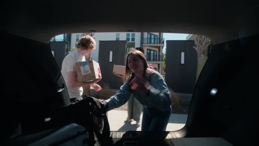 View from inside a car trunk as three excited young friends unload boxes and luggage in slow motion on moving day