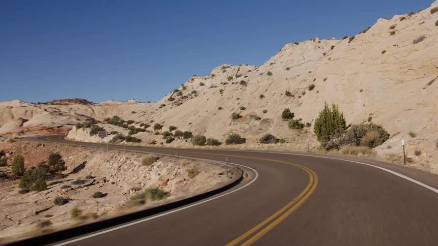 An aerial shot pulls back from a scenic desert highway before transitioning into a fast-paced POV drive through the rocky Utah landscape
