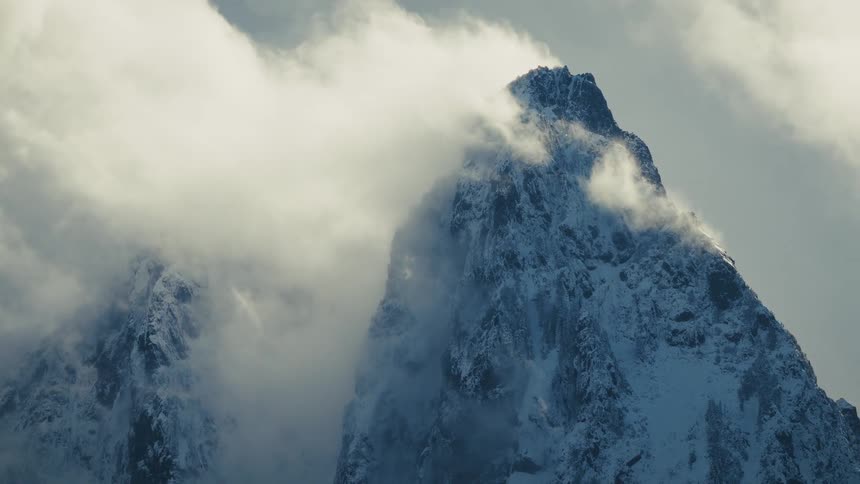 Wind and clouds move dramatically across a majestic, snow-covered mountain peak