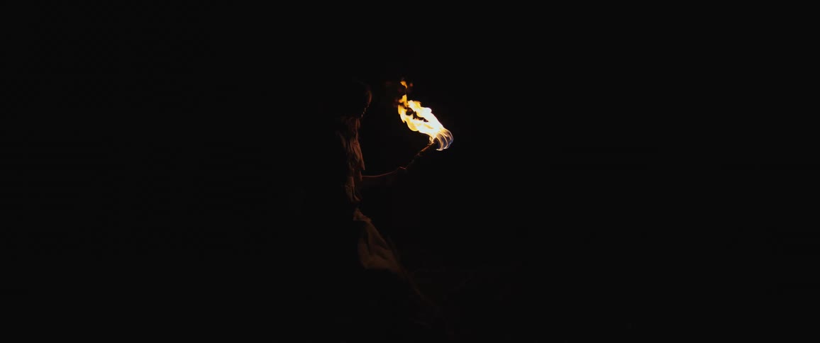 A mysterious silhouette of a person holds a flaming torch, the only source of light in the pitch-black darkness