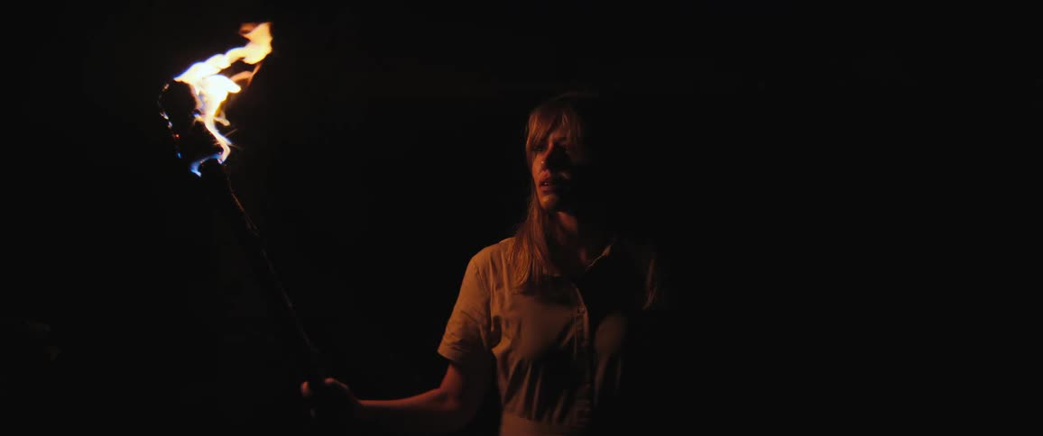 A cautious woman explorer holds a flaming torch, peering into the surrounding darkness at night