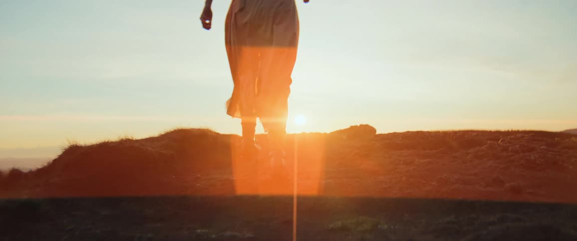 A cinematic slow-motion close-up of a woman's boots as she walks up a grassy hill towards the beautiful golden sunrise