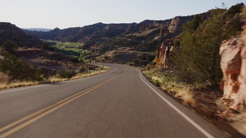 A point-of-view shot of a smooth drive on a winding highway through a stunning red rock canyon under a bright sky