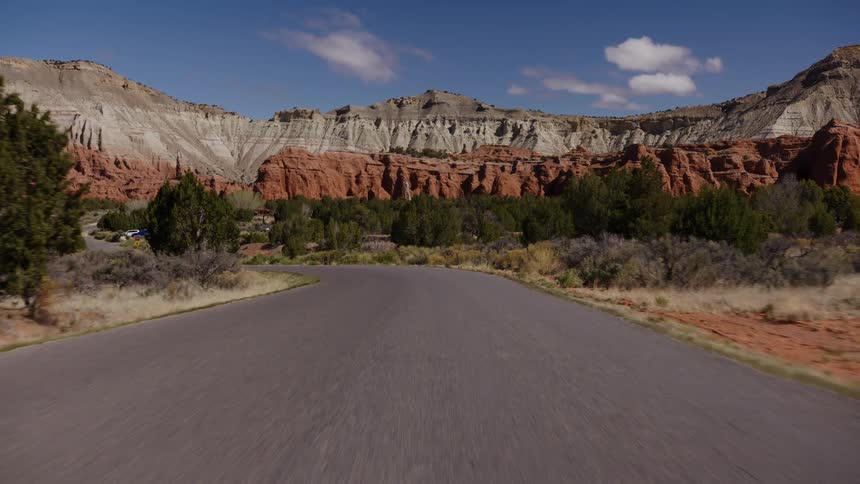 Driving slowly along a winding desert road towards the majestic, multi-colored rock formations of a Utah state park on a beautiful day