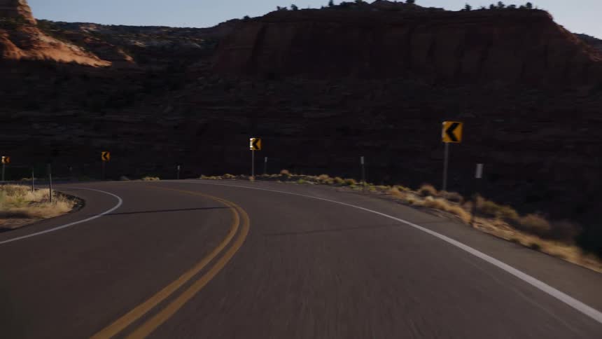 A point-of-view driving shot on a winding highway through a stunning red rock desert canyon at sunset
