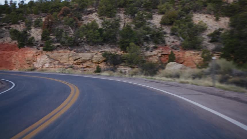 A point-of-view shot driving along a winding highway through a red rock canyon landscape in the desert