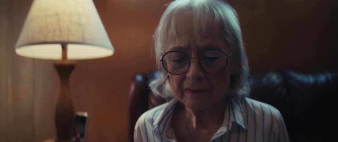 Close-up of a sad, elderly woman in glasses as she reads a healthcare information brochure