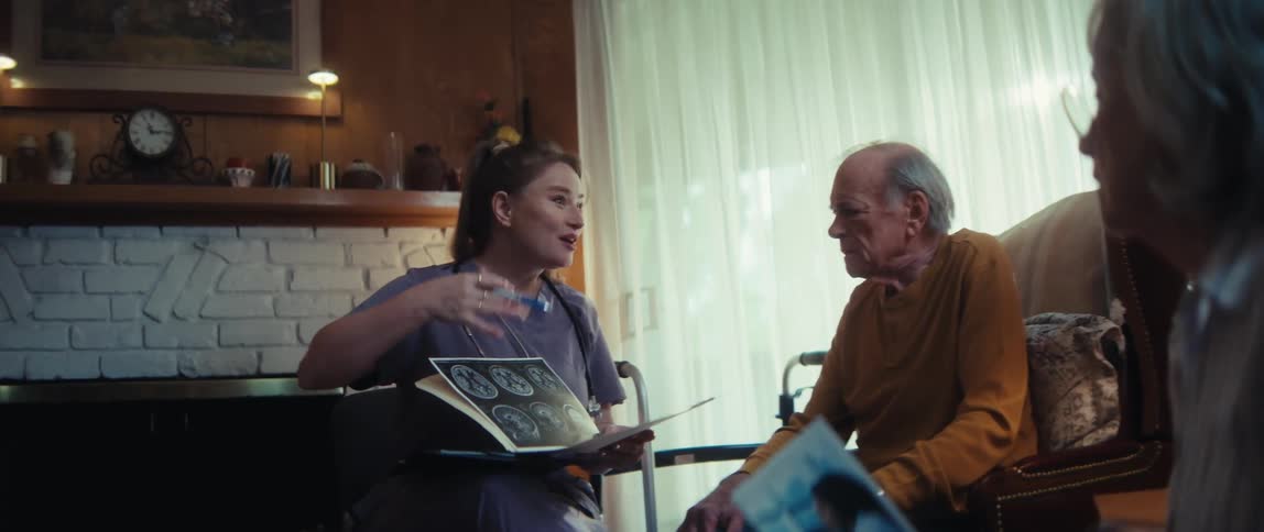 A friendly nurse in scrubs compassionately explains brain scan results to an elderly man and his wife during a home visit