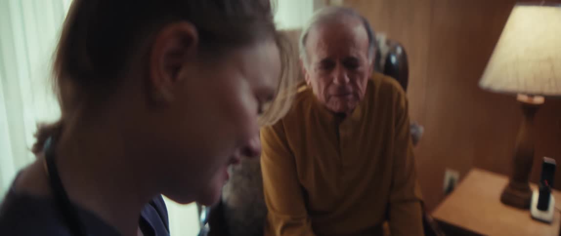 A compassionate nurse cares for an elderly man in his home, with a slow rack focus from her caring expression to his