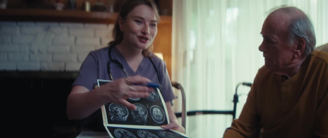 A compassionate nurse reviews brain scan results with a concerned elderly man and his wife during a home visit