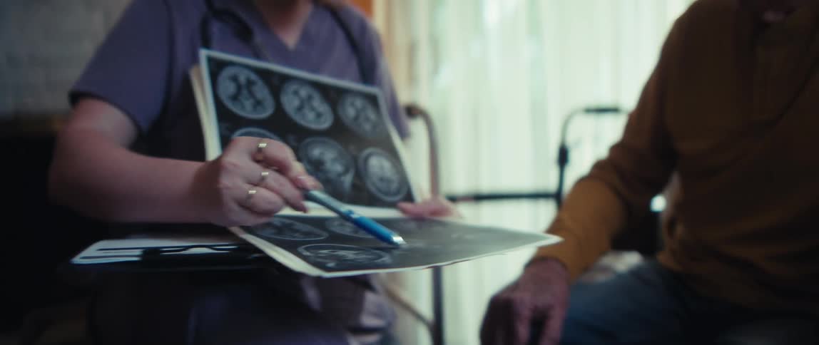 A caring home-care nurse gently explains a brain MRI scan to a concerned elderly woman and her husband in their living room