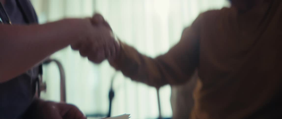 A slow-motion close-up shot shows a doctor and a patient shaking hands in agreement after a consultation