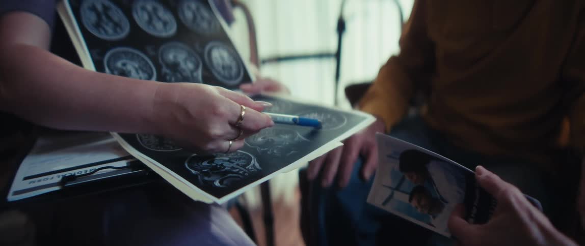 A healthcare professional points to a brain scan while explaining a diagnosis to an elderly patient