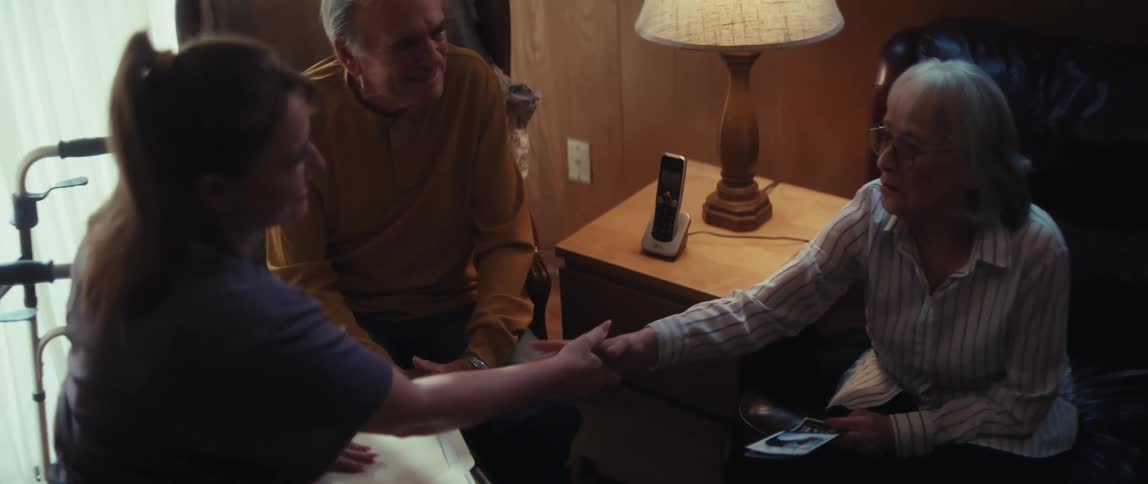 A compassionate healthcare worker shakes hands with an elderly woman during a home visit with her husband