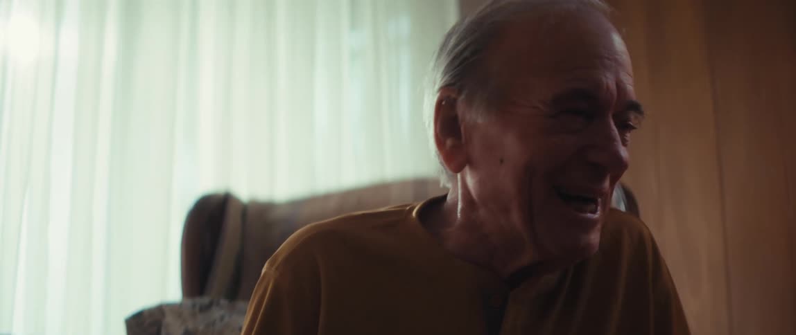 A heartwarming close-up shot focuses on an elderly man's face as he breaks into a joyful laugh while talking with his caregiver