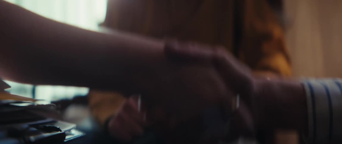 A female caregiver and an elderly man share a warm handshake, culminating in the man's joyful laughter in a sunlit room