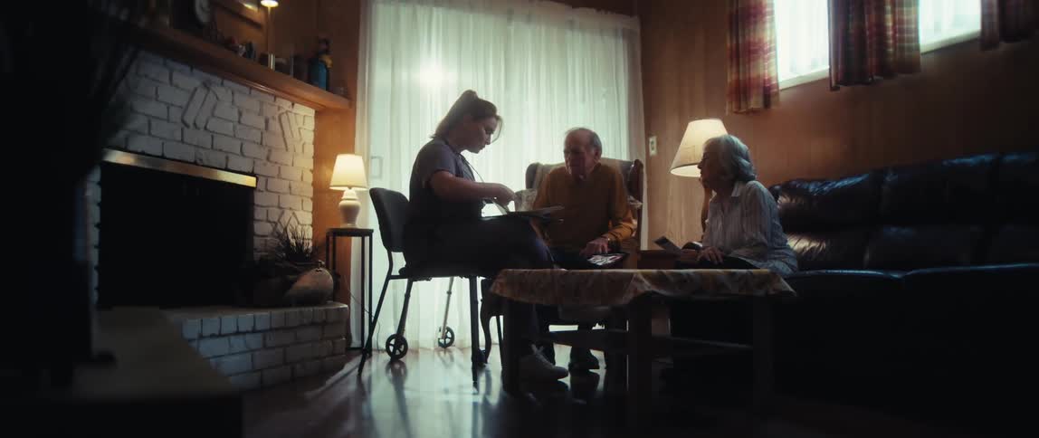 A compassionate in-home caregiver shares memories from a photo album with an elderly couple in their cozy living room