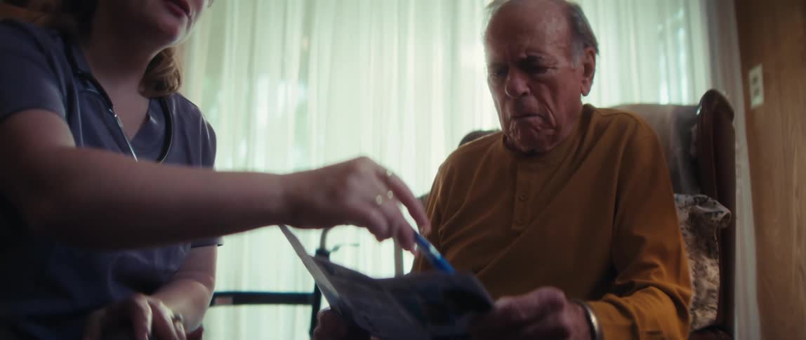 A home healthcare nurse carefully explains the details of a medical brochure to an elderly man sitting in his armchair