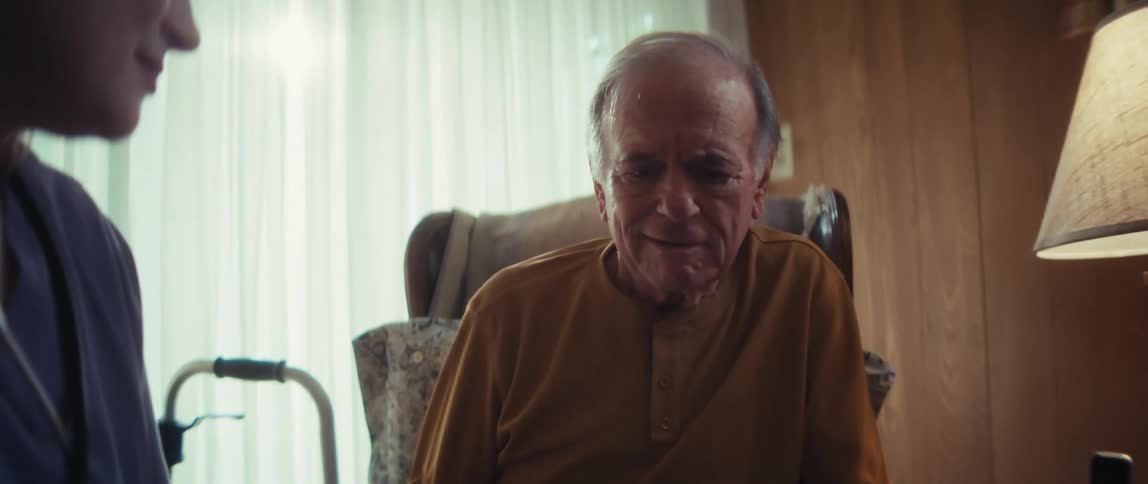 A compassionate home healthcare nurse explains care options from a brochure to an elderly man and his wife in their living room