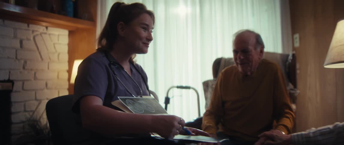 A friendly nurse delivers positive news while reviewing brain scan results with a smiling elderly couple in their cozy living room
