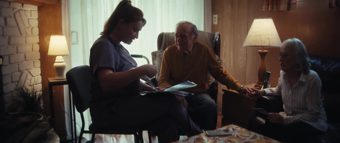A compassionate home healthcare nurse consults with an elderly couple, reviewing paperwork in their living room