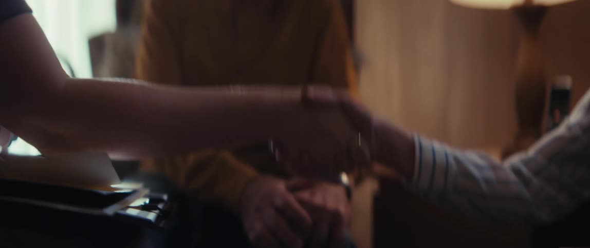 A caregiver shakes hands with a smiling elderly man in his home, offering comfort and support