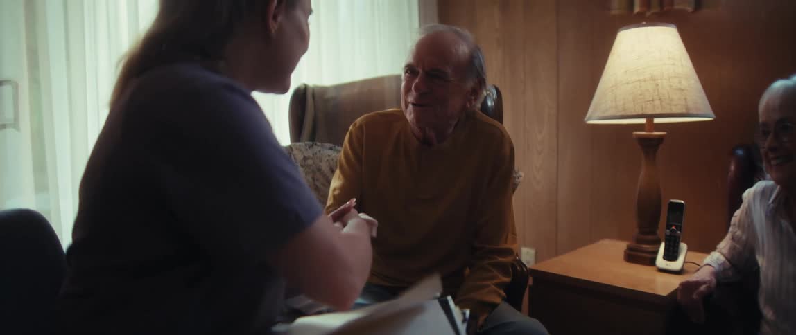 A compassionate nurse delivers good news to a senior couple during a home visit, shaking their hands and leaving them with smiles