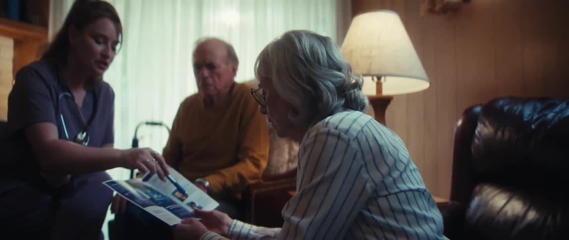 A home care nurse reviews a healthcare brochure with a concerned elderly couple in their living room