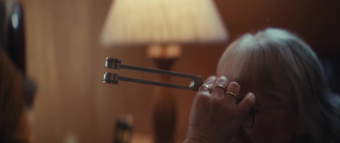 A therapist administers a relaxing sound healing treatment to an elderly woman using a tuning fork in a softly lit room