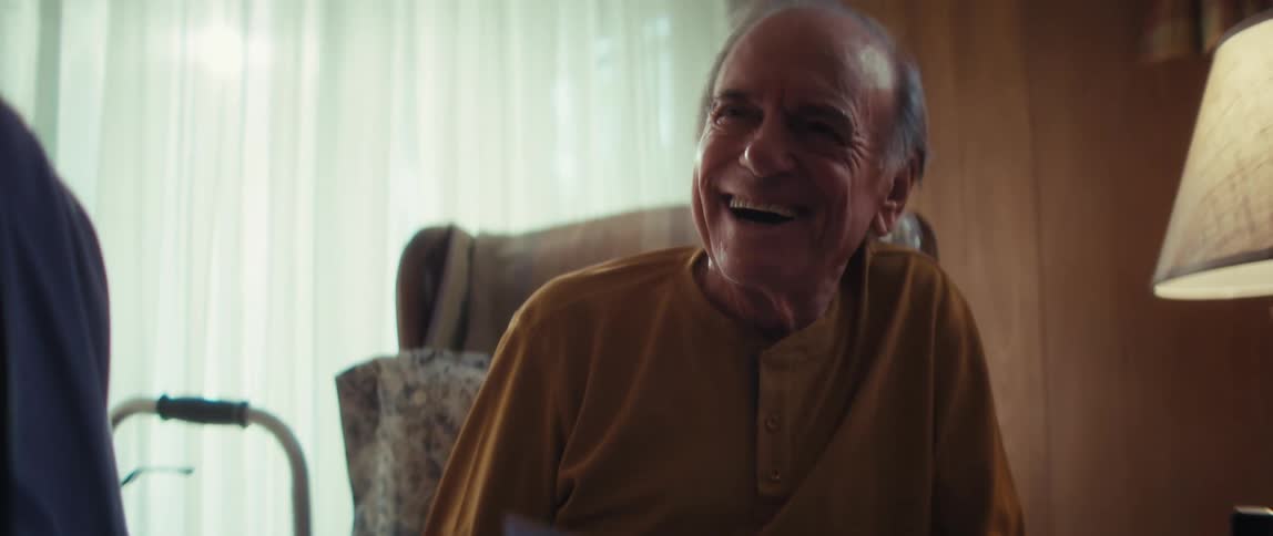A slow motion rack focus reveals a happy elderly man laughing while a caregiver explains a healthcare brochure