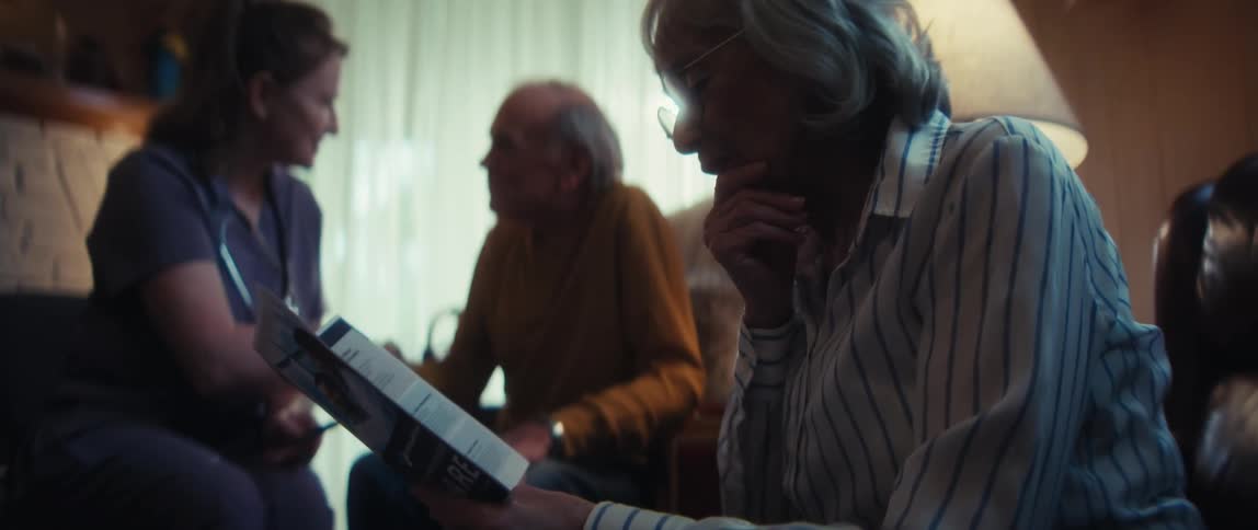 A kind home healthcare nurse reviews a medical brochure with an elderly couple in their cozy living room