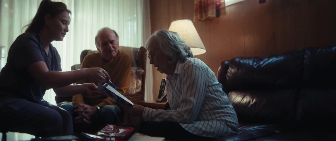 A home healthcare nurse explains medical options to an elderly couple from a brochure in their living room