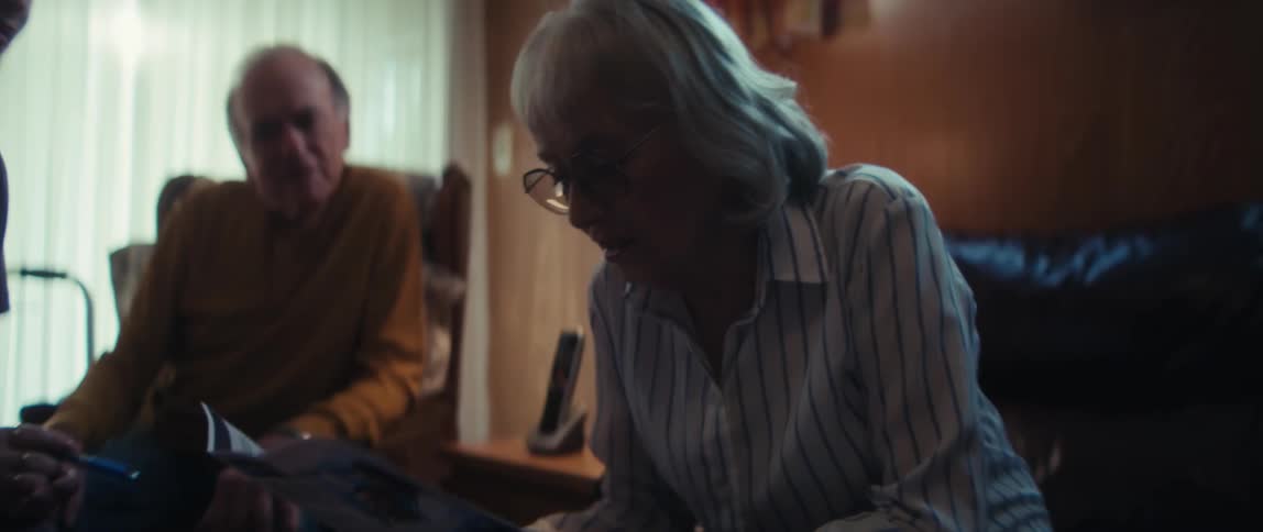 A compassionate home healthcare nurse discusses care options with an elderly couple in their living room, showing them a brochure