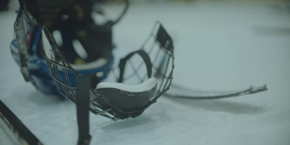 A close-up shot of a blue ice hockey helmet with snow in the chin cup, abandoned on the ice rink