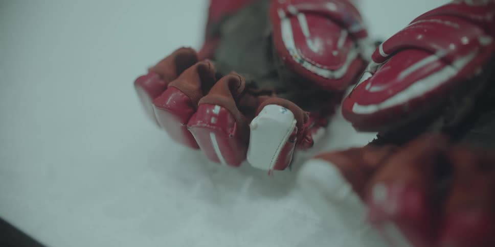 A close-up shot of worn red and white hockey gloves resting on the ice as steam drifts across them