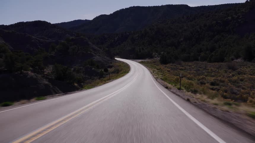 A smooth, first-person view of a drive along a winding country road through a scenic mountain landscape